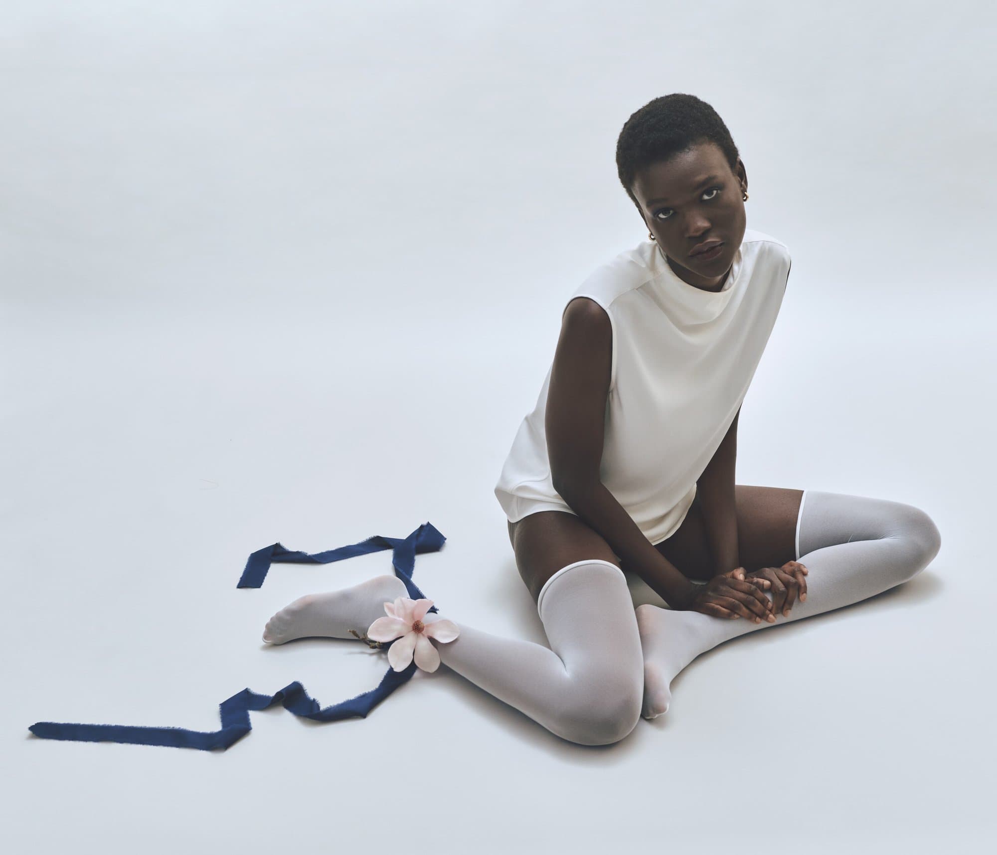 Portrait of a young African woman in a white top and thigh-high socks sitting with her legs crossed, a blue ribbon with a pink flower.