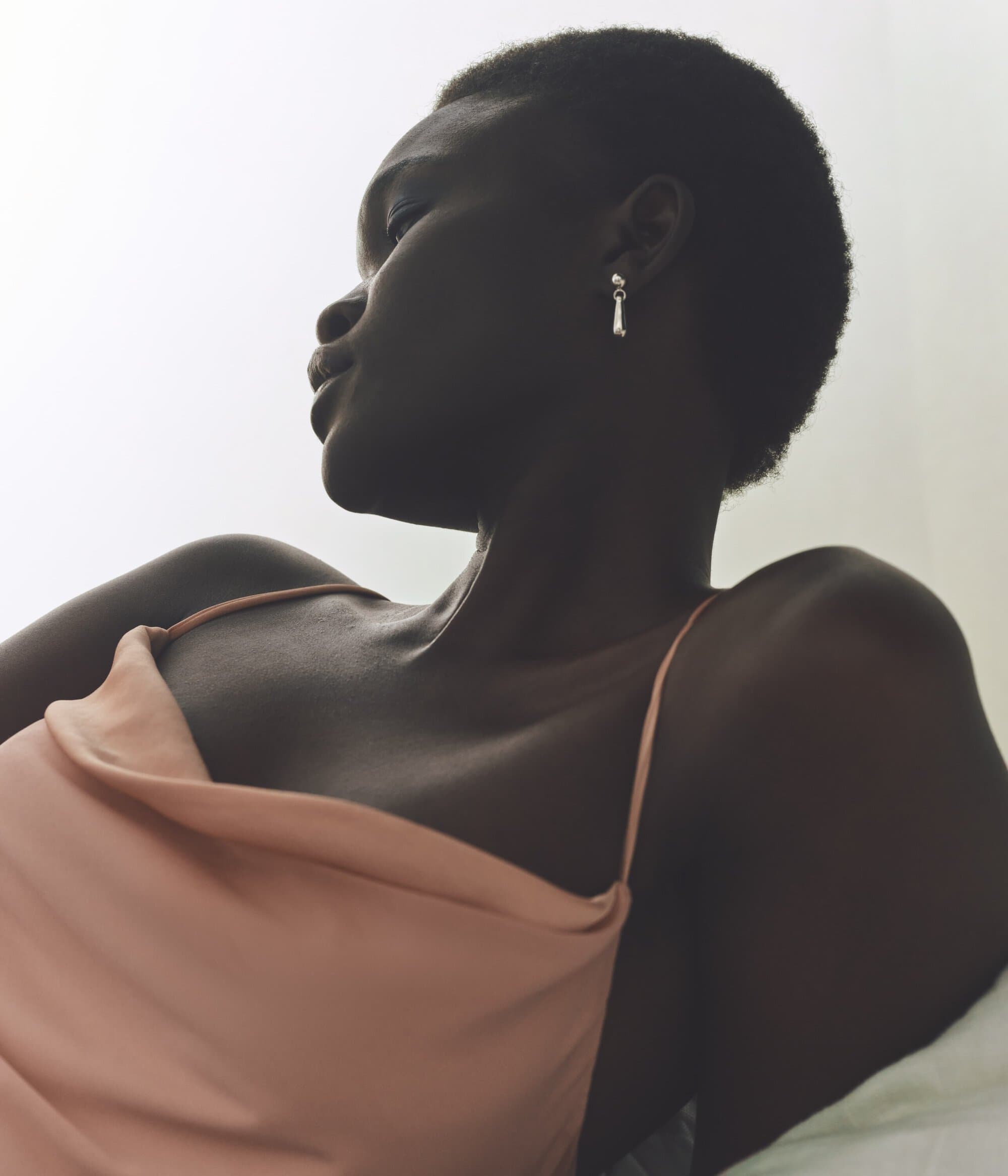 Portrait of a dark-skinned woman with short hair wearing a peach-colored top and earrings, captured with natural lighting in a studio.