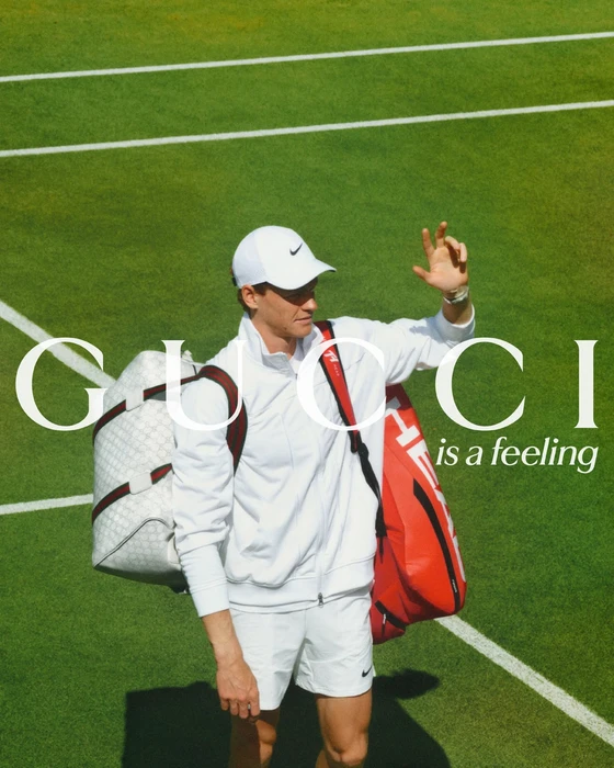 Tennis player Jannik Sinner in white sportswear carrying two sports bags on a green tennis court for Gucci Spring 2024 campaign