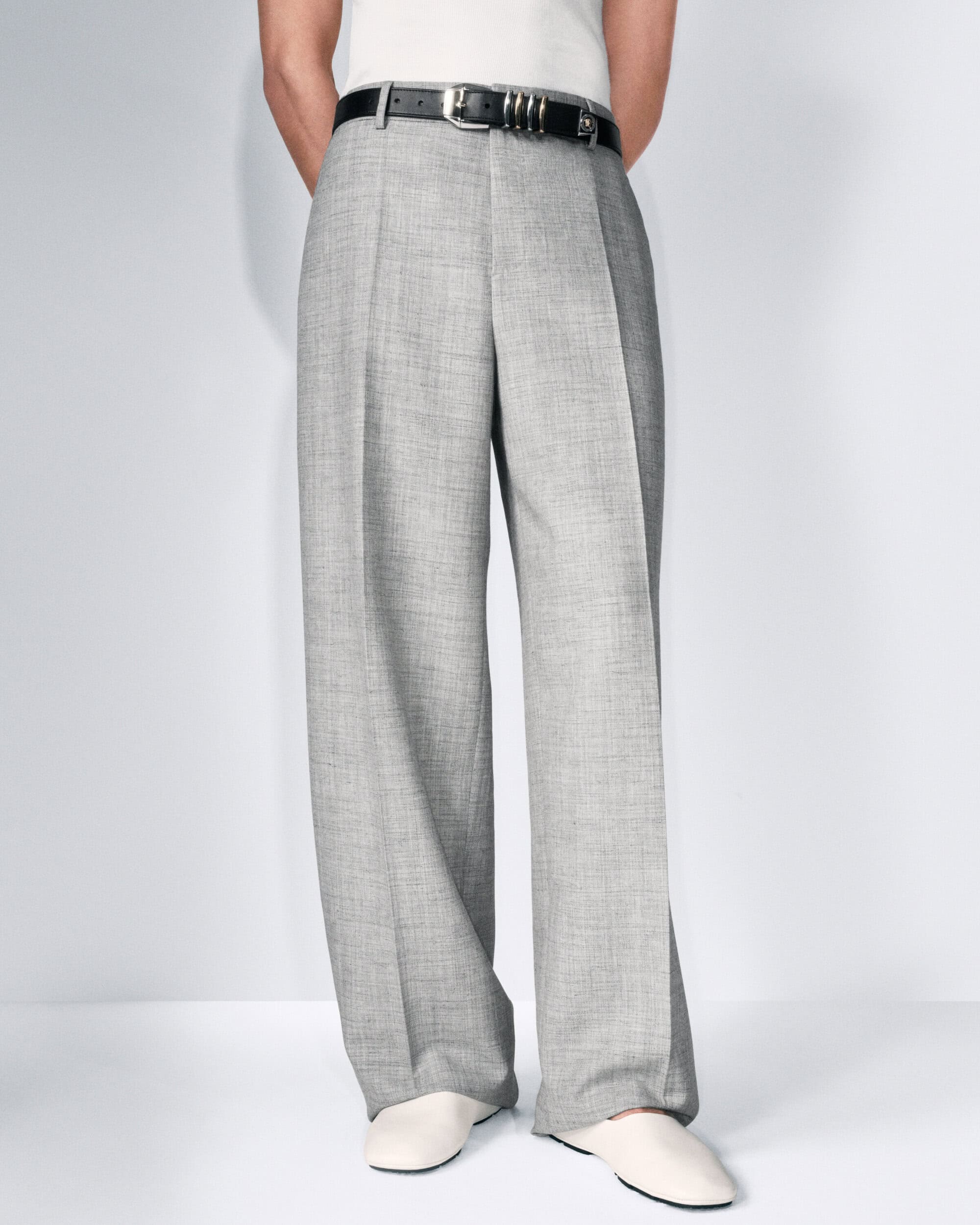 Light grey, wide-leg trousers with a black belt and off-white shoes are shown on a person against a plain white background.