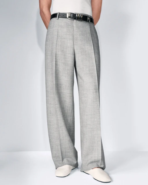 Light grey, wide-leg trousers with a black belt and off-white shoes are shown on a person against a plain white background.