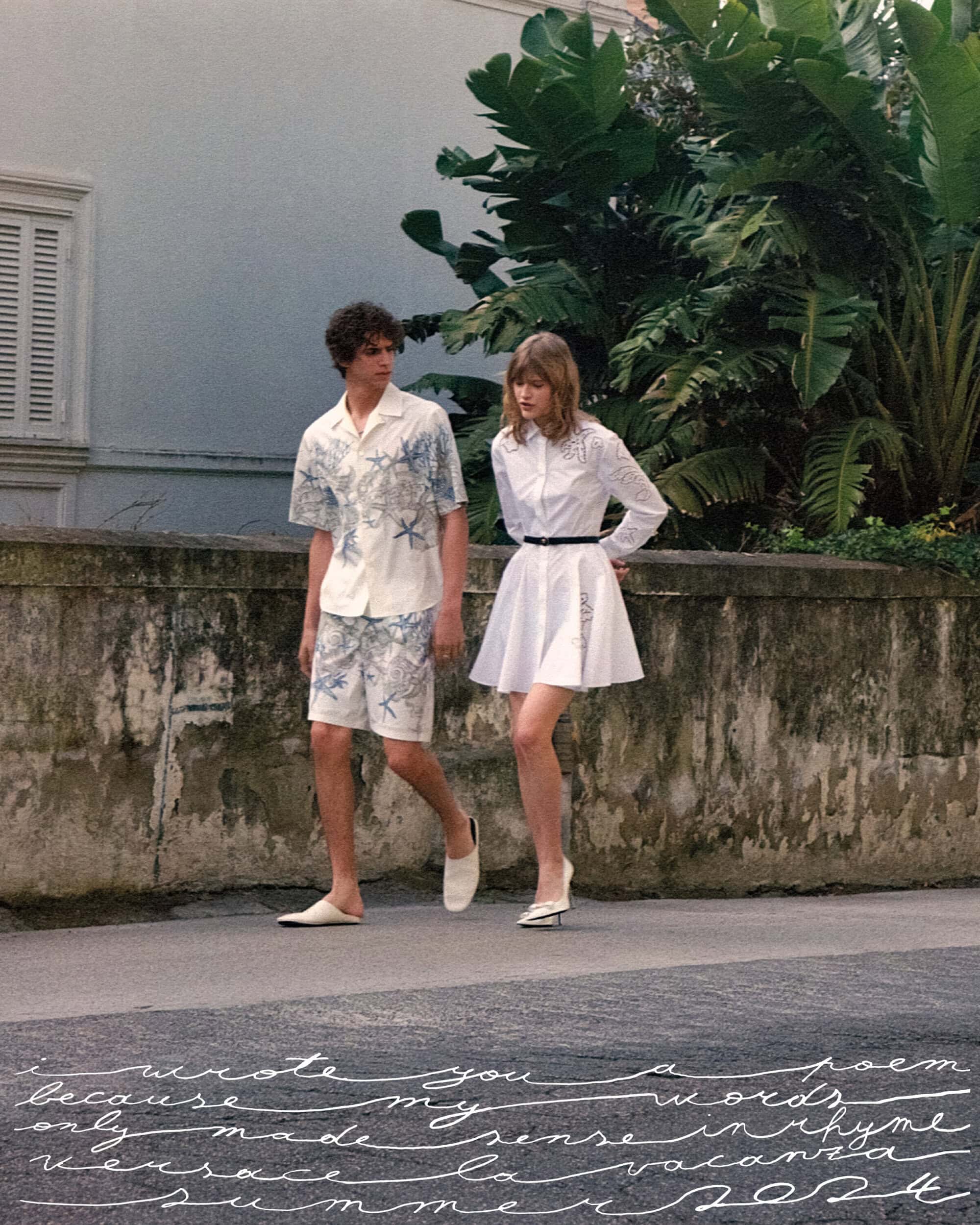 Two fashion models wearing white, patterned summer outfits walking outdoors near building and greenery, showcasing summer collection.