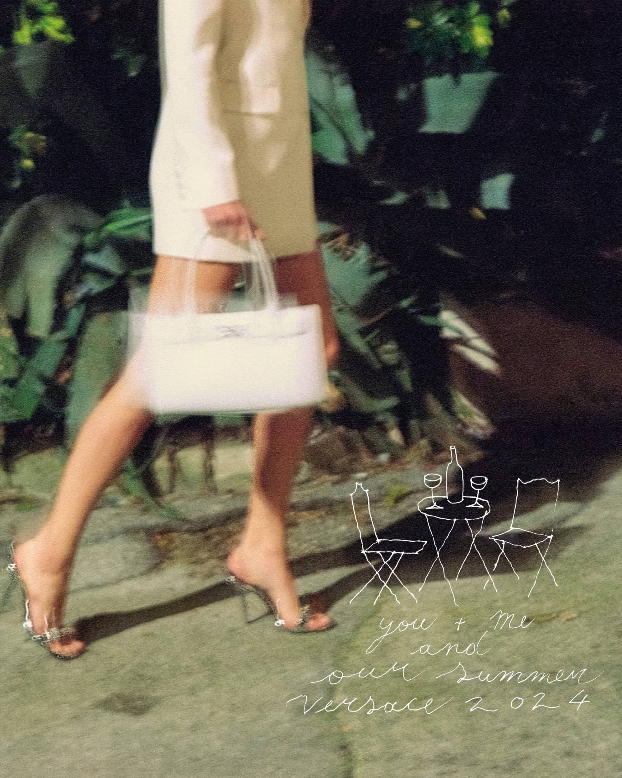 Fashion shot of a woman walking in a cream-colored suit holding a white purse with high heels and tropical foliage in the background.