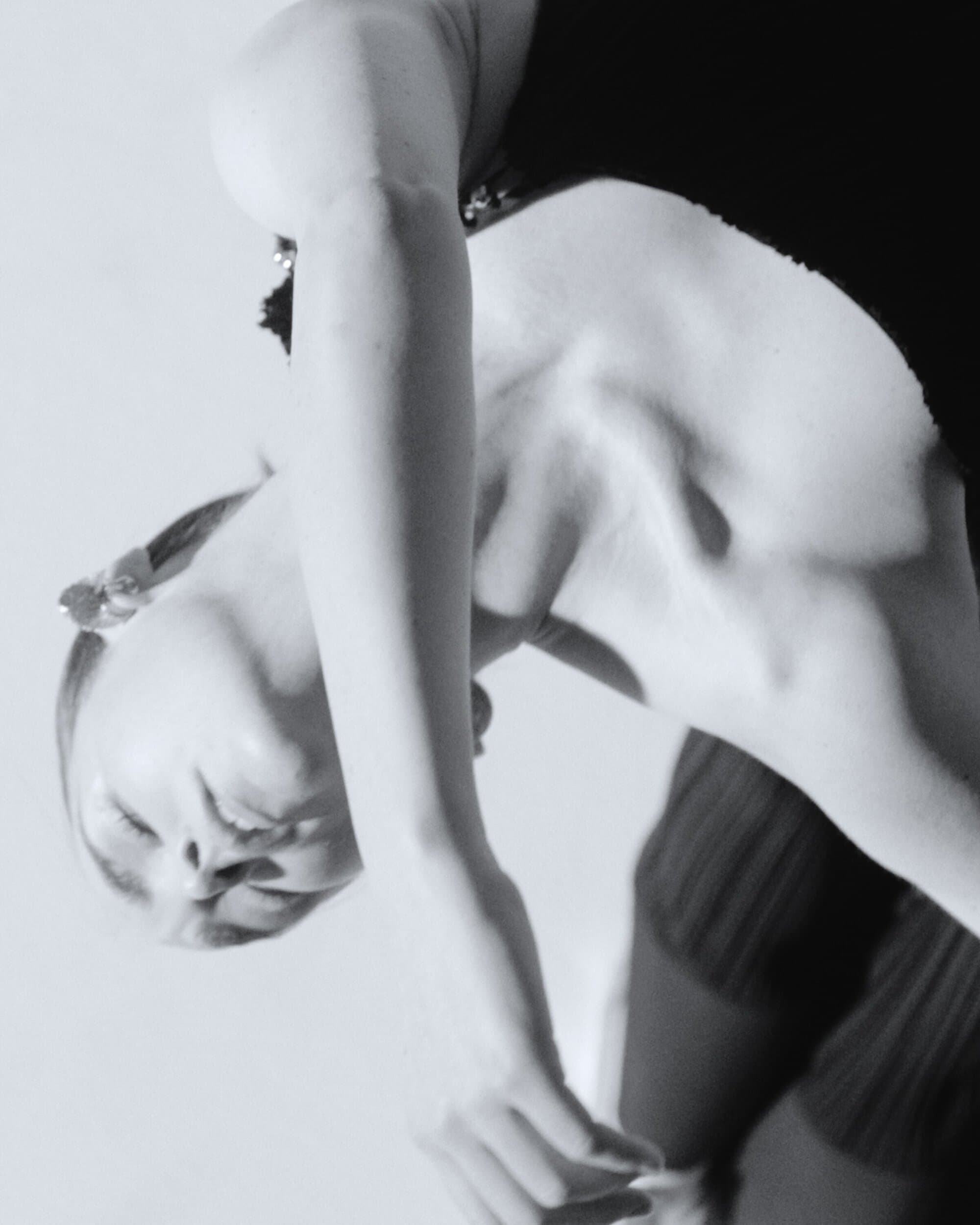 Monochrome portrait of a fair-skinned woman with eyes closed, wearing a dark sleeveless top against a light backdrop.