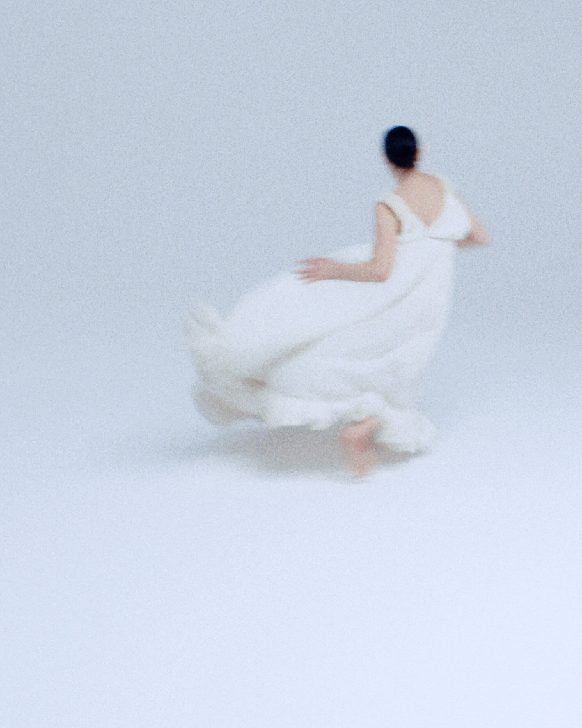 An adult female in motion, wearing a flowing white dress, stands out against a bright white background, viewed from a low angle.