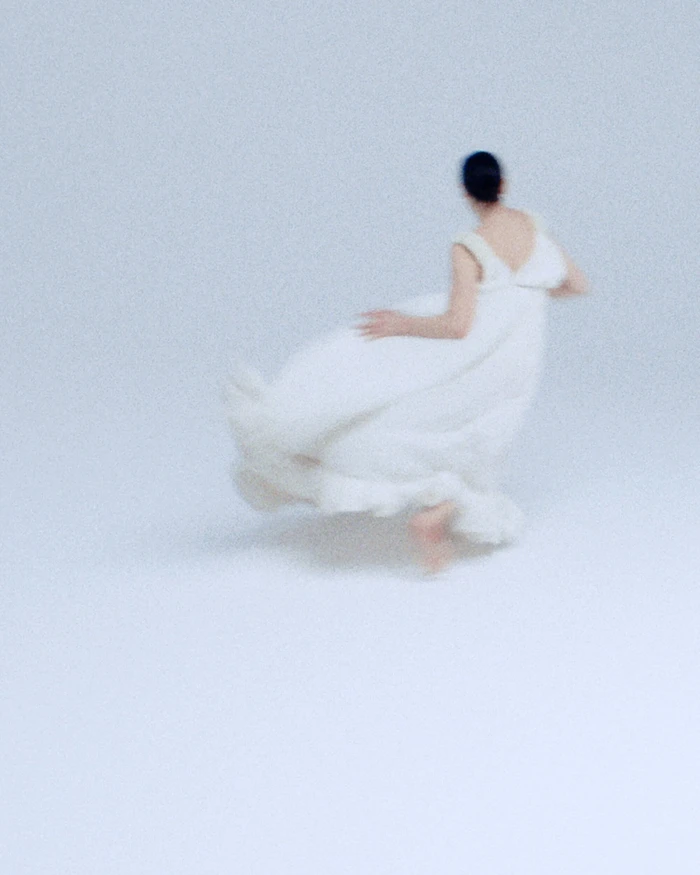 Motion-blurred model in a flowing white dress captured in motion against a seamless white background for Lanvin.