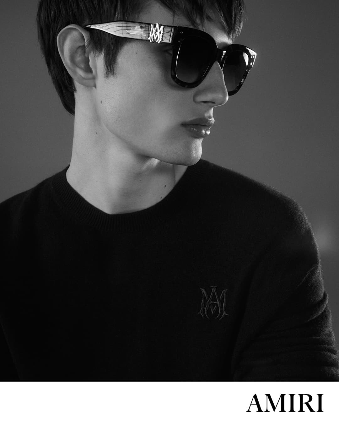 Close-up portrait of a man wearing dark sunglasses and a black sweater for Amiri Core ad campaign