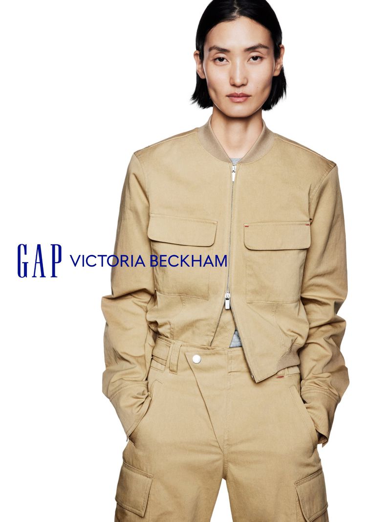 A woman with dark hair wearing a beige utility jacket and matching trousers poses against a plain white background for Gap and Victoria Beckham.