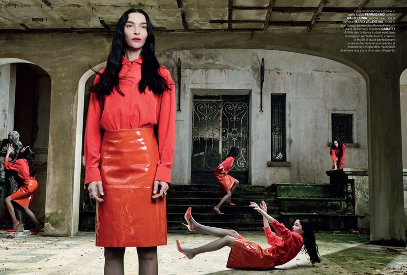Fashion editorial shot of a woman in a red blouse and skirt, mirrored by multiple clones in the setting of a weathered stone building.