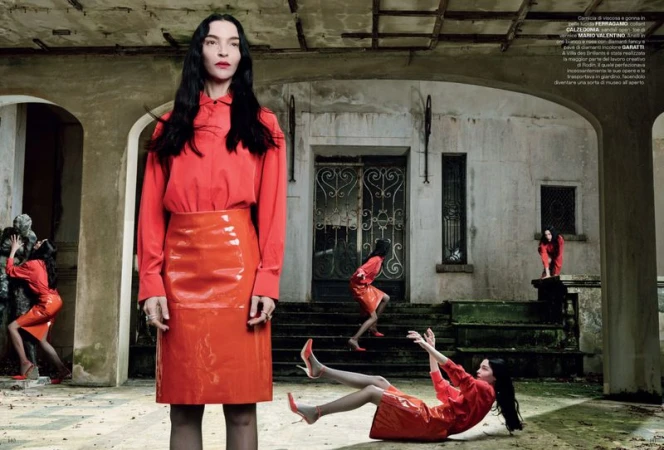 Fashion editorial shot of a woman in a red blouse and skirt, mirrored by multiple clones in the setting of a weathered stone building.