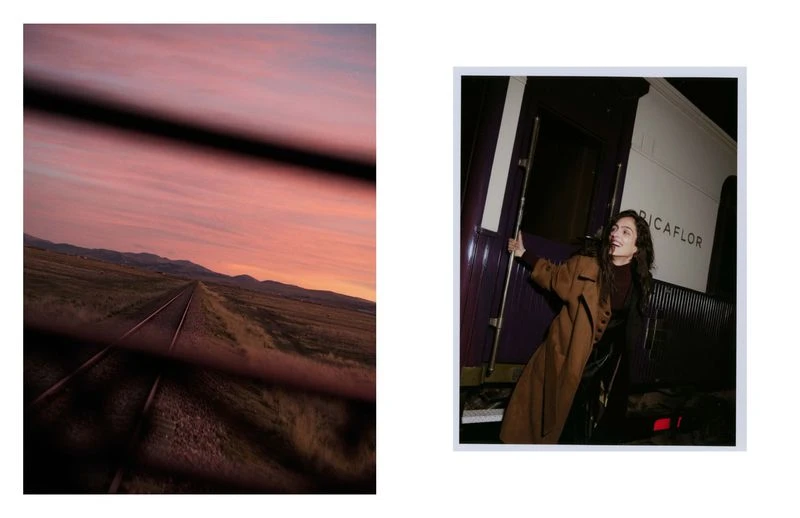 Model poses by train car on tracks extending to horizon, framed by train window bars, at sunset with colorful sky in background.