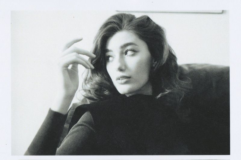 Black and white portrait of a thoughtful woman with wavy hair, wearing a dark turtleneck, and posing indoors, looking off to the side.