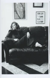 Woman in dark clothing lounging on a dark leather sofa in an interior setting for Herdes Magazine editorial project Nuit et Jour.