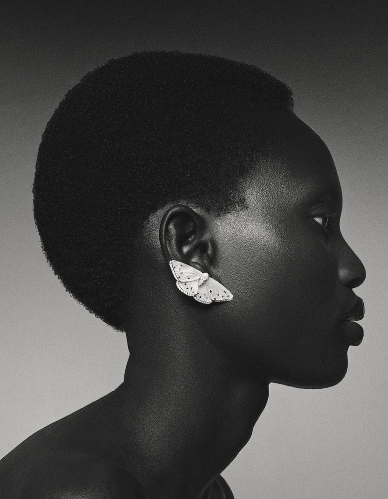 Profile portrait of a Black woman wearing butterfly earring in a beauty shot with a neutral grey background in studio lighting.