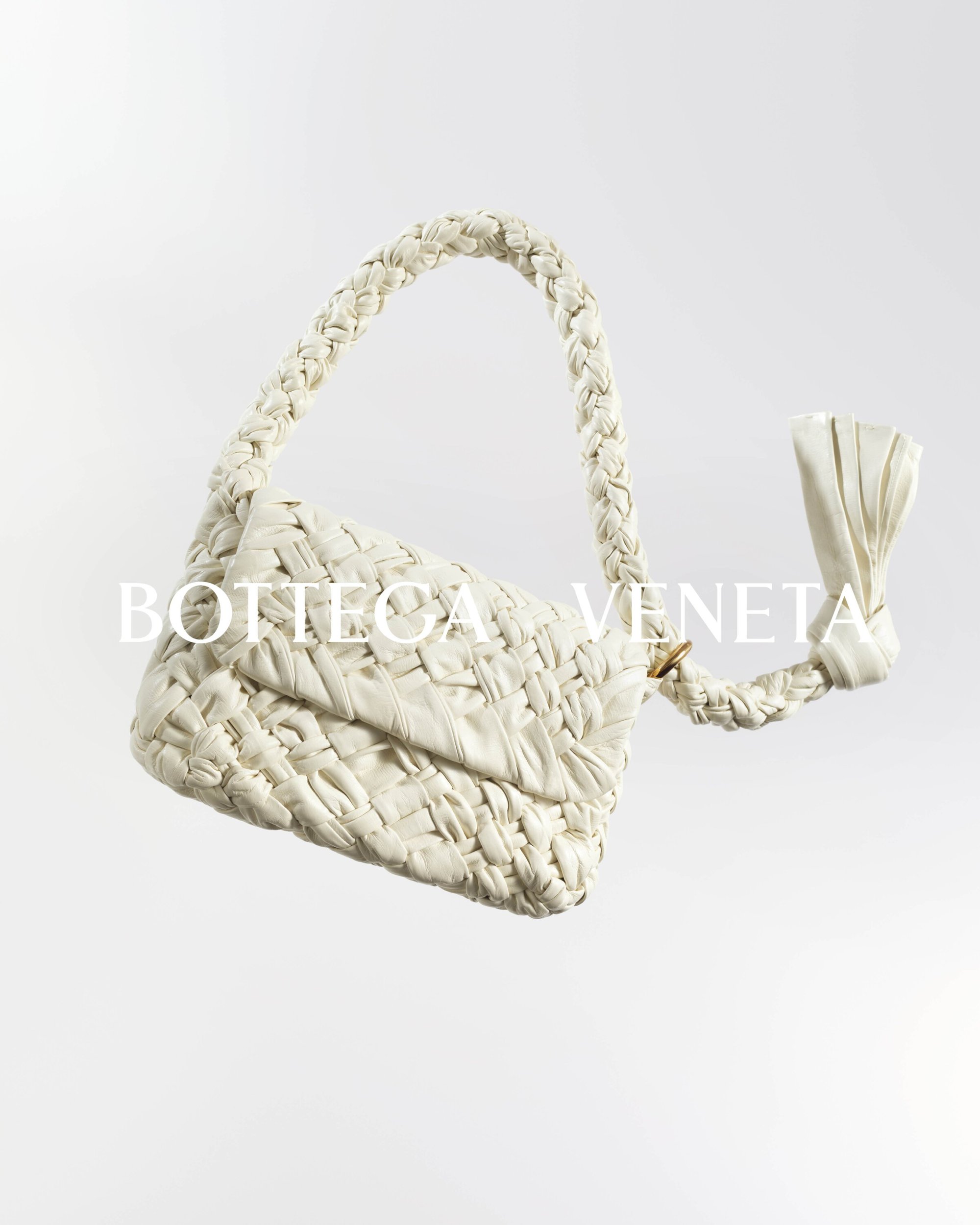 White Bottega Veneta woven leather handbag with a twisted handle and a knotted detail, presented against a bright white backdrop.