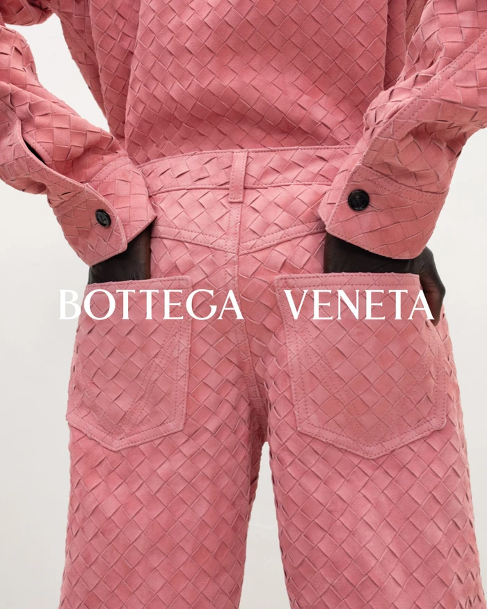 Close-up shot from behind of a person wearing a pink woven leather shirt and matching trousers against a solid background