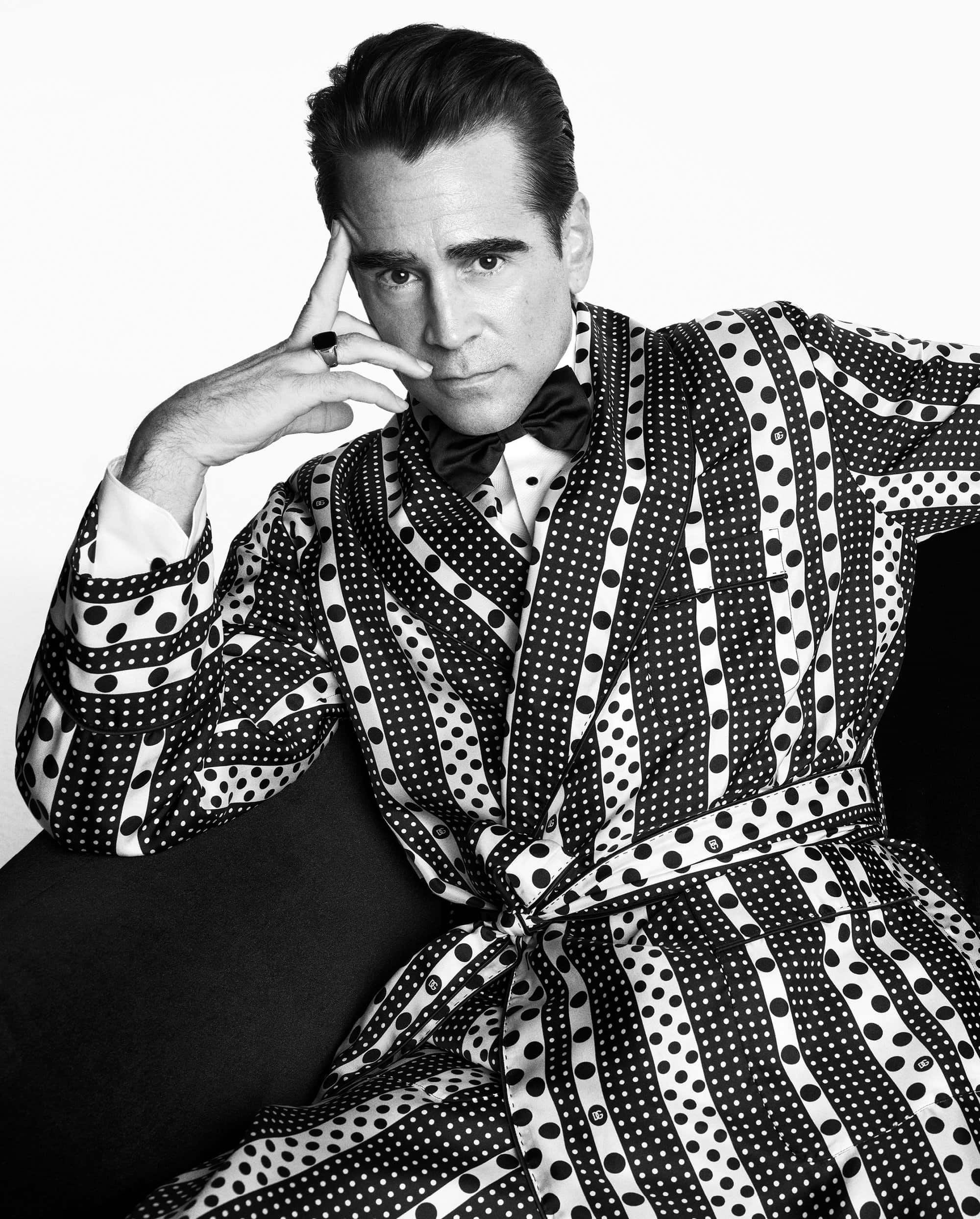Black and white portrait of adult male in patterned robe and bow tie, hand to his head, gazing seriously into the camera.