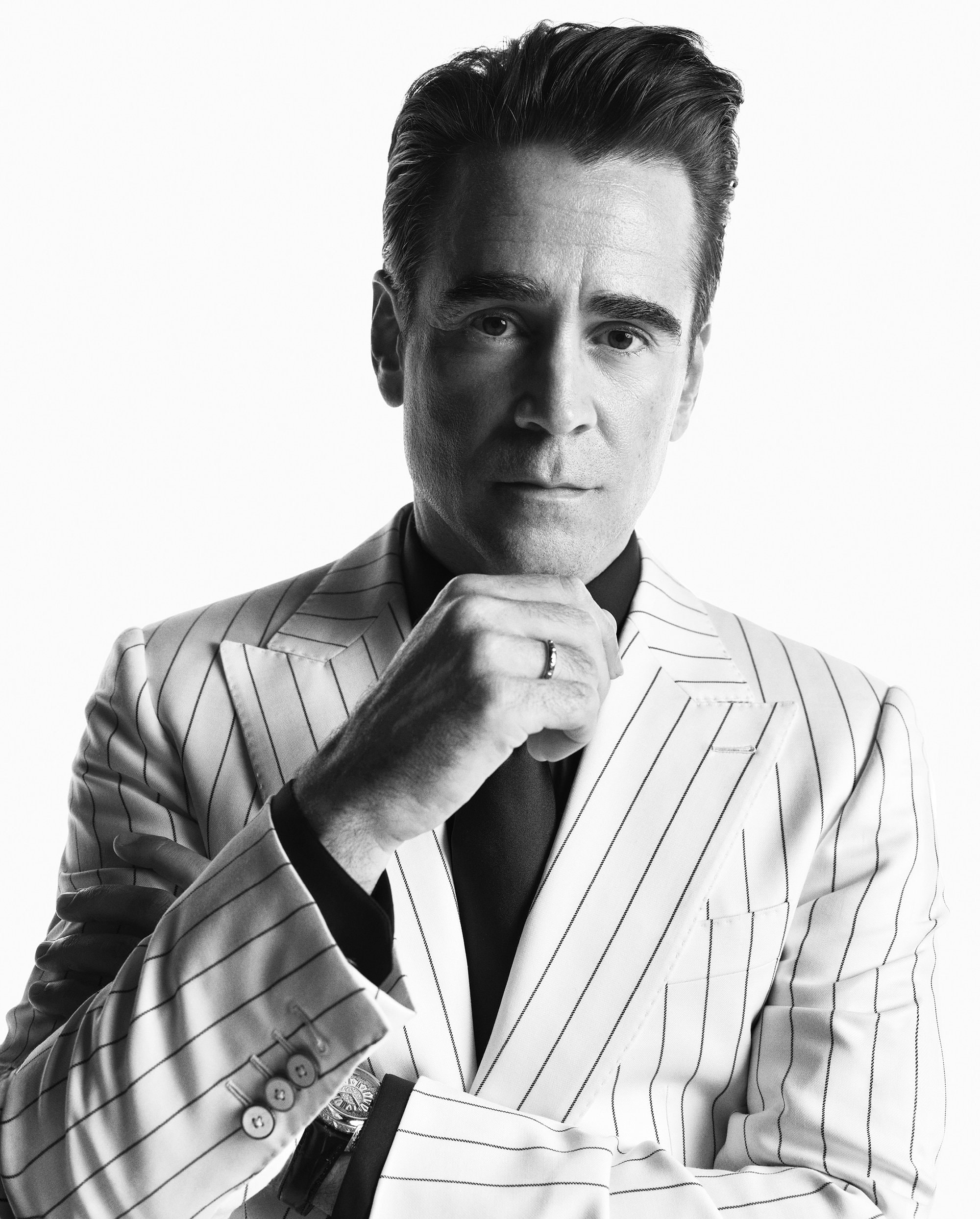 Black and white portrait of a man in a pinstripe suit with his hand near his chin, wearing a wedding band, against a white background.