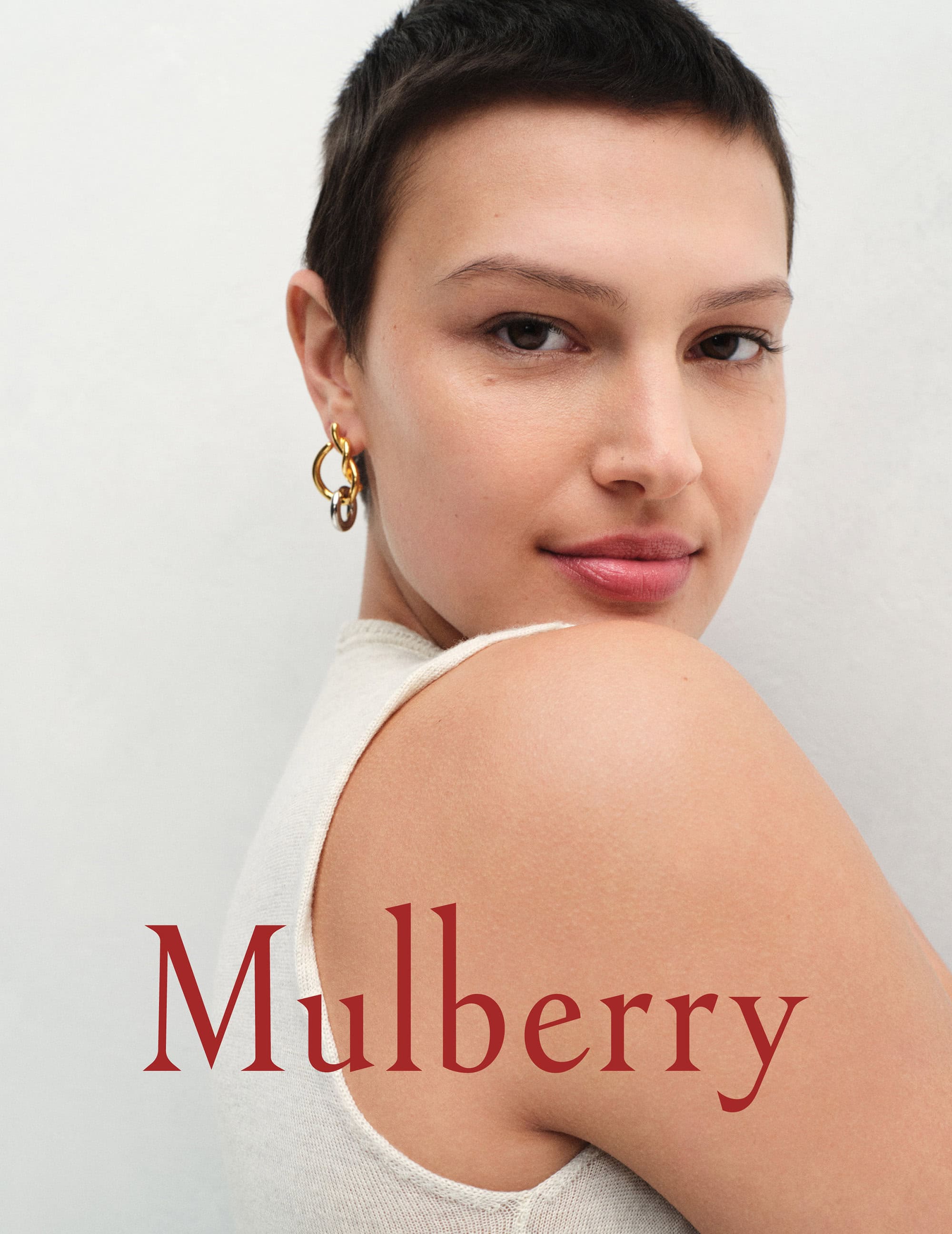 Close-up of a woman with short brown hair and gold hoop earrings, with the Mulberry brand logo in the lower left.