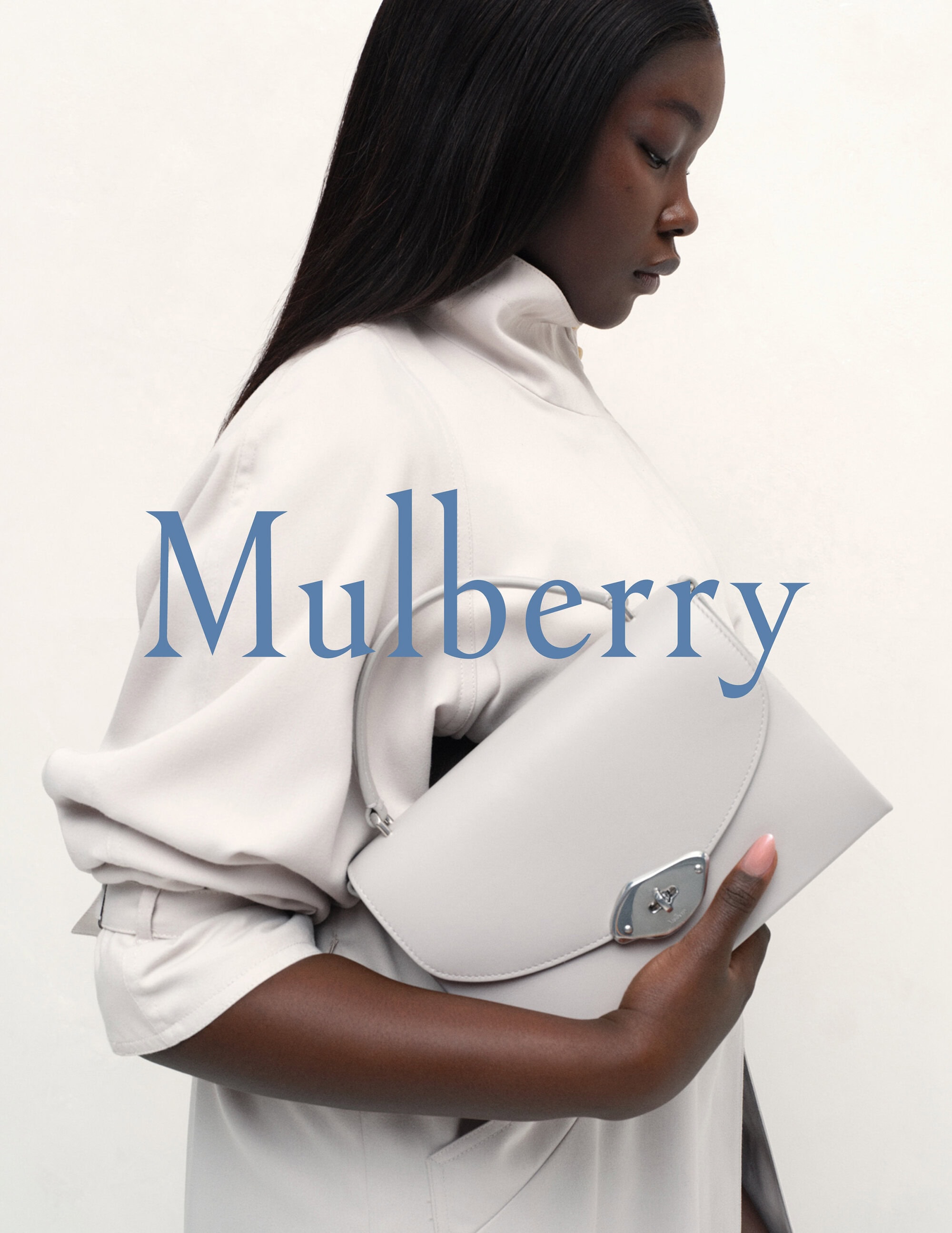 Fashion shot featuring a dark-skinned woman holding a light grey leather purse in a studio with soft, neutral lighting.