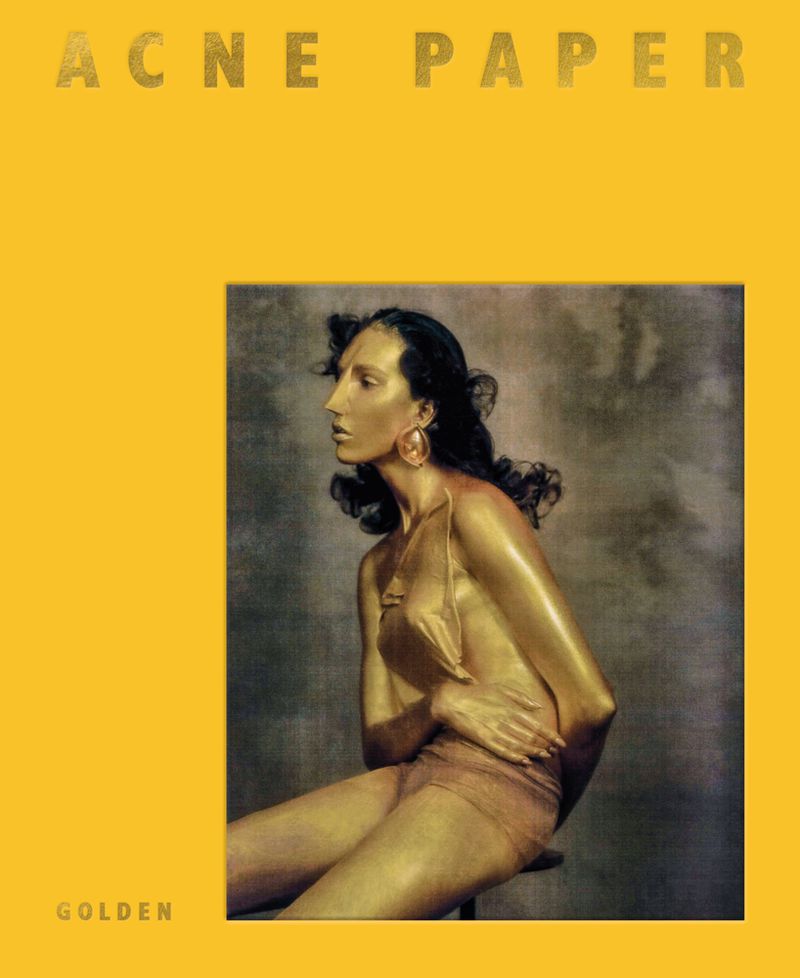 Profile view of an adult female with tan skin and dark hair, sitting on a stool against a grey background. Part of an Acne Paper advertisement.