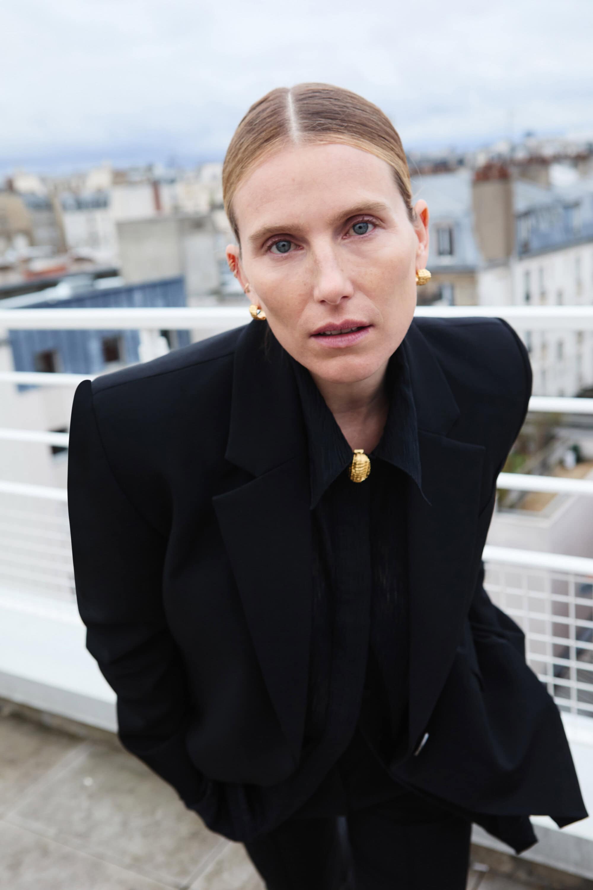 Model Dree Hemingway in a black blazer and matching shirt against a rooftop background for Camilla and Marc