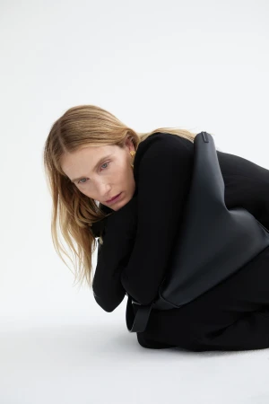 Model Dree Hemingway posing with a black handbag against a bright white background for Camilla and Marc