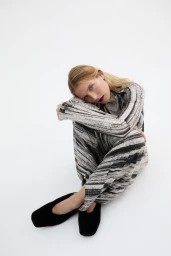 Model Dree Hemingway seated on a white studio floor wearing a patterned monochrome outfit and black shoes