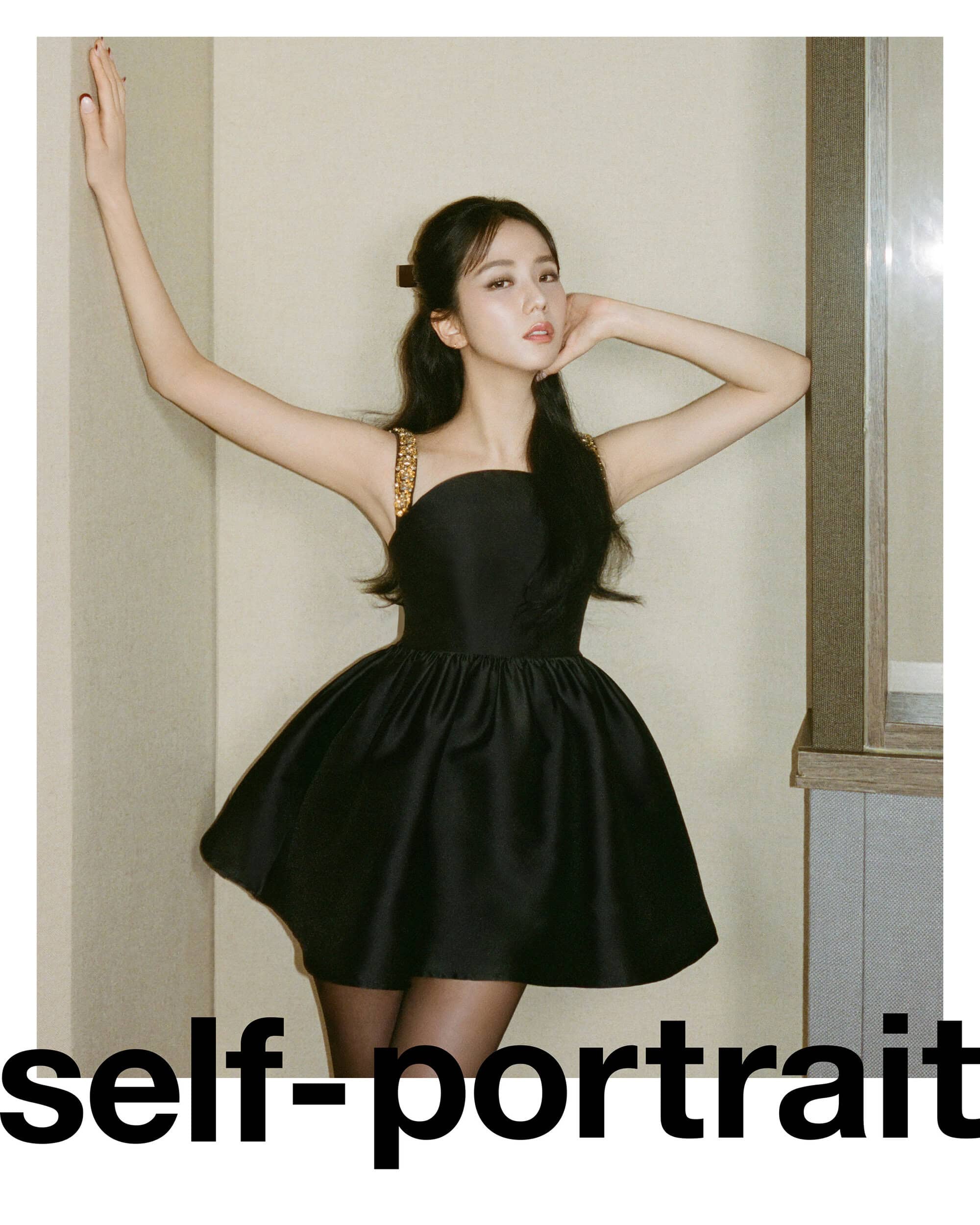 Portrait of a woman in a black dress posing against a neutral background, with her arms raised, showing elegance and style.