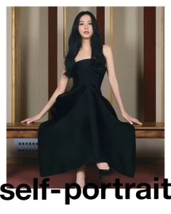 Jisoo seated wearing a black strapless midi dress against a wood panel wall for Self-Portrait Pre-Fall 2024