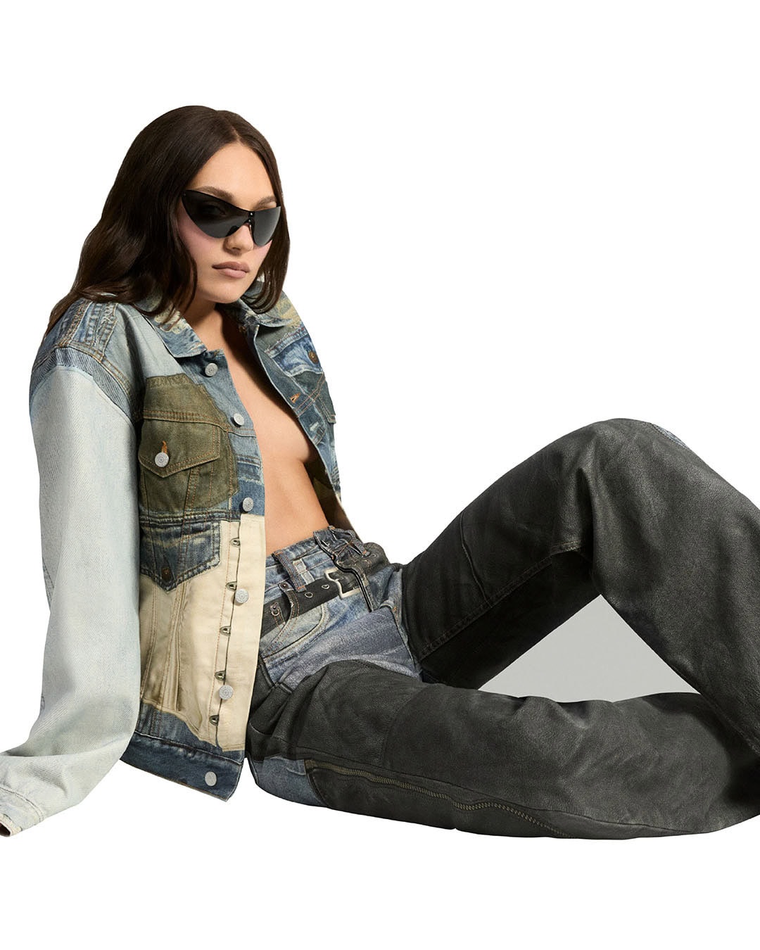 Adult female poses in a photo studio wearing a patchwork denim jacket, light-wash jeans, and sunglasses against a white backdrop.