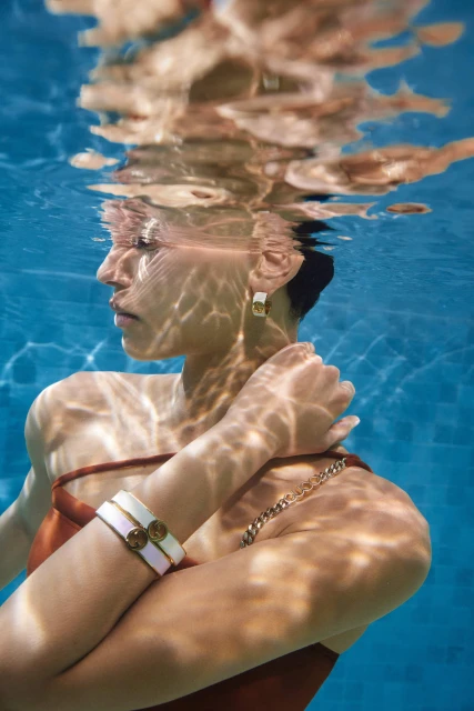 Underwater portrait of a woman in a rust-colored swimsuit and jewelry, reflecting on the surface of the water in a swimming pool.