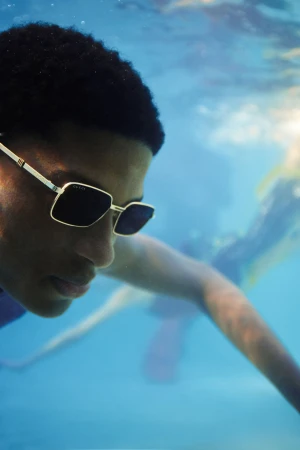 Underwater portrait of a person wearing Gucci sunglasses, with other people blurred in the background, and underwater sun rays visible.