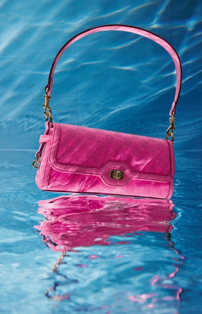Pink handbag with a handle reflected in water against a blue background. Studio shot. Fashion photography. Product shot.
