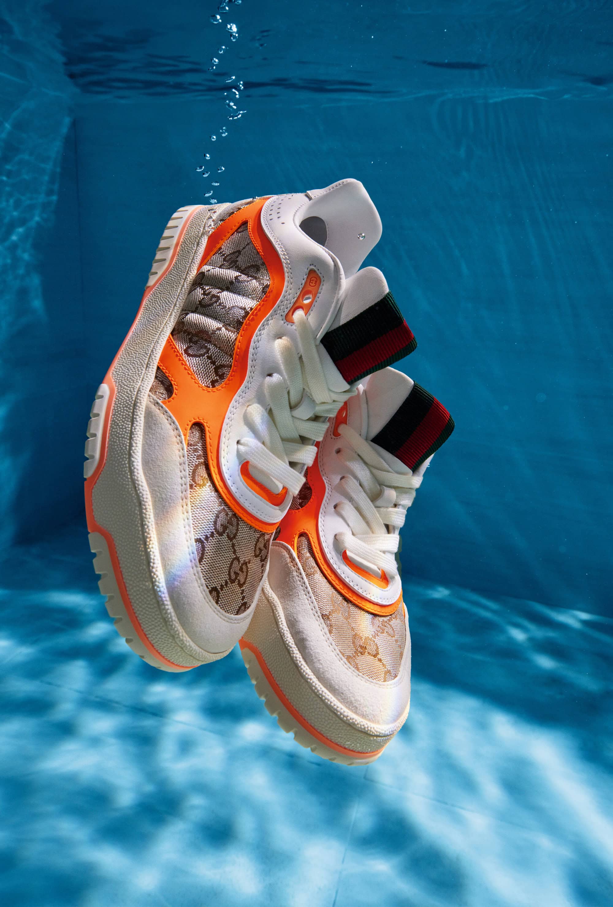 Luxury Gucci sneakers suspended in blue water, creating an eye-catching product shot with a clean and vibrant aesthetic.