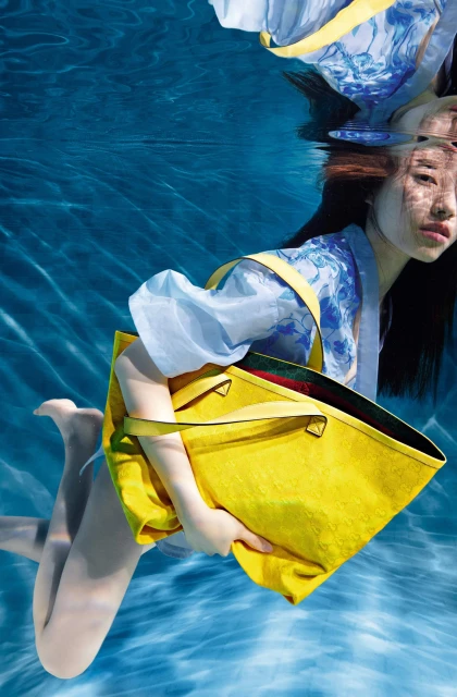 Underwater shot of a woman in a kimono holding a yellow tote bag, captured in an underwater fashion photography style, vibrant and surreal.