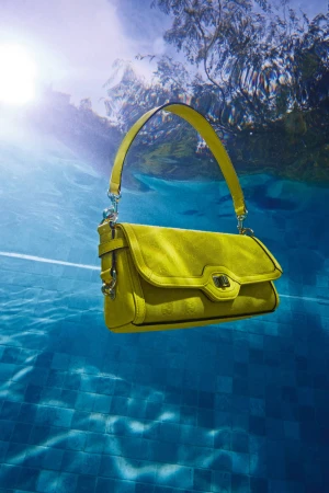 Chartreuse designer purse floats in clear blue swimming pool water with sunlight filtering through the underwater setting.