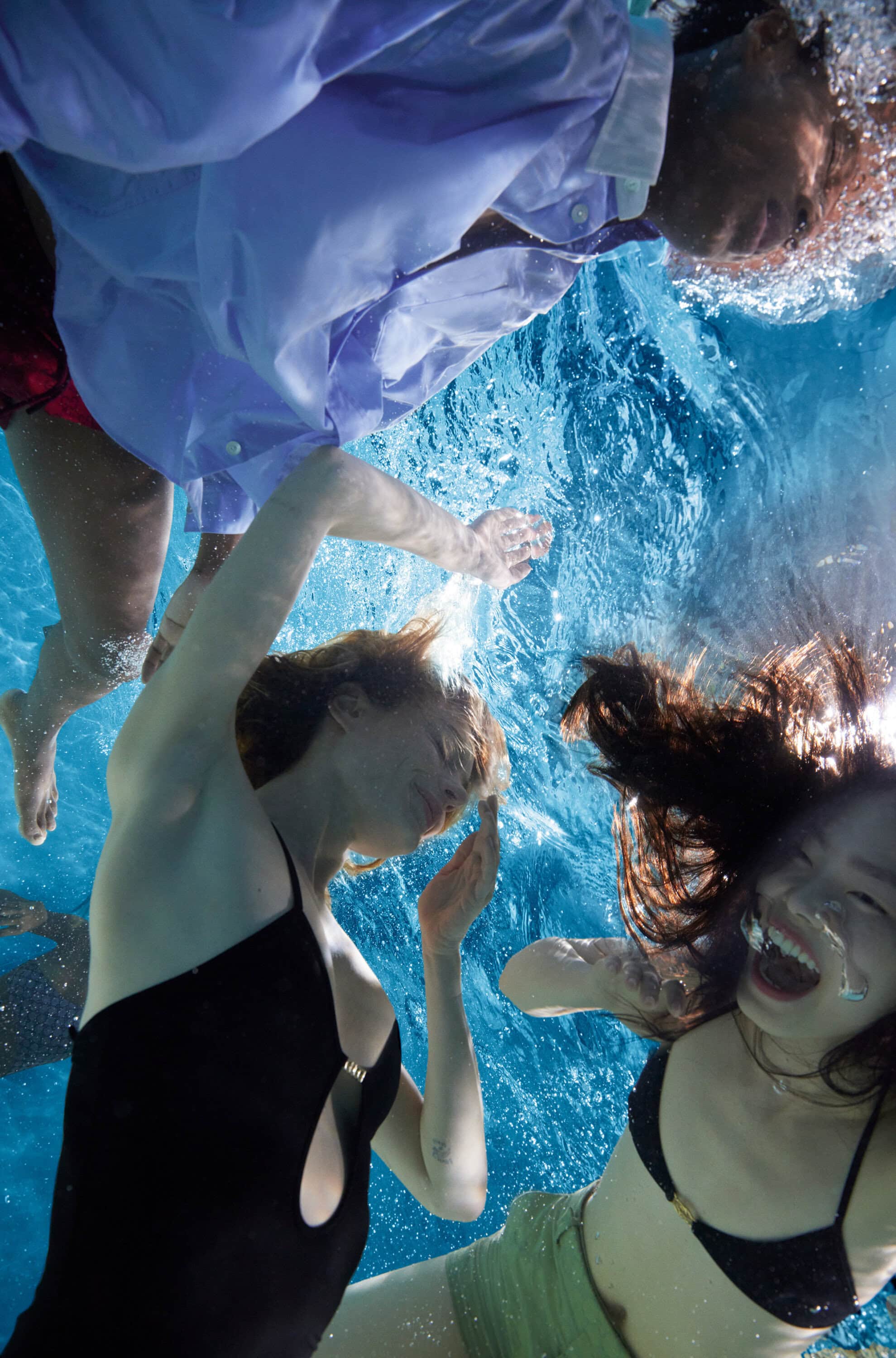 Underwater view of four people swimming in a pool, capturing a serene and active moment with clear blue water and natural light.