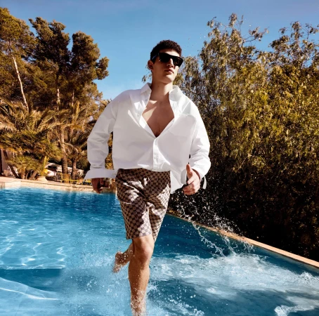 Man wearing sunglasses and a white shirt running through an outdoor swimming pool splashing water
