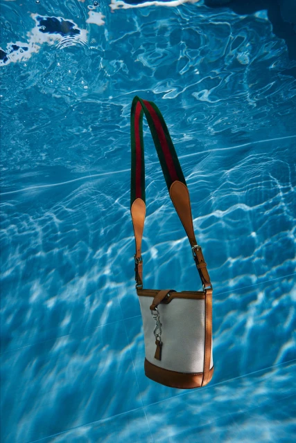 Fashionable handbag with leather trim floats in clear blue water, illuminated by refracted light for a striking underwater shot.
