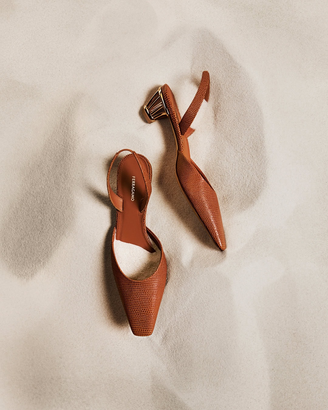 A pair of light brown slingback heels are arranged on a textured cream background in a high-angle product shot.