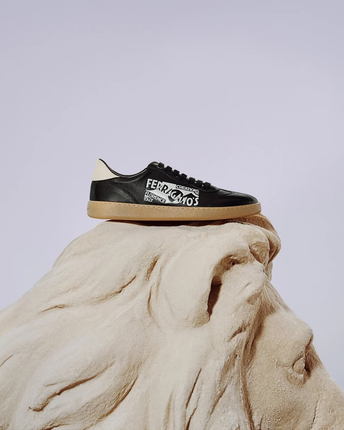 Black leather sneaker with white branding resting on top of a carved stone lion sculpture