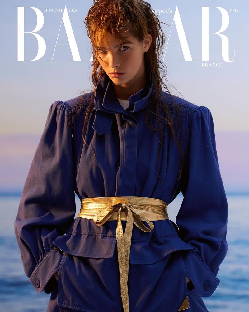 Fashion editorial featuring a woman with wet hair wearing a blue jacket and gold belt against a blurred background in Harper's Bazaar France.