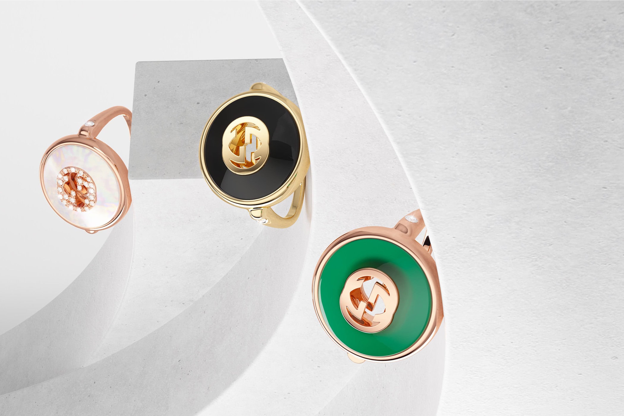 Studio product shot of three elegant Gucci rings in gold, rose gold, black, white, and green with iconic interlocking G logo.