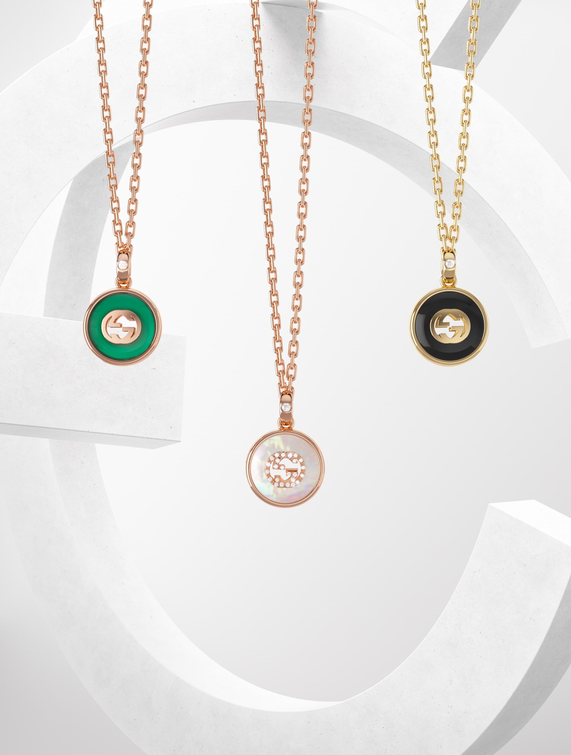 Three necklaces with round pendants in green, rose gold, and gold on a white surface, showcasing fine jewelry.