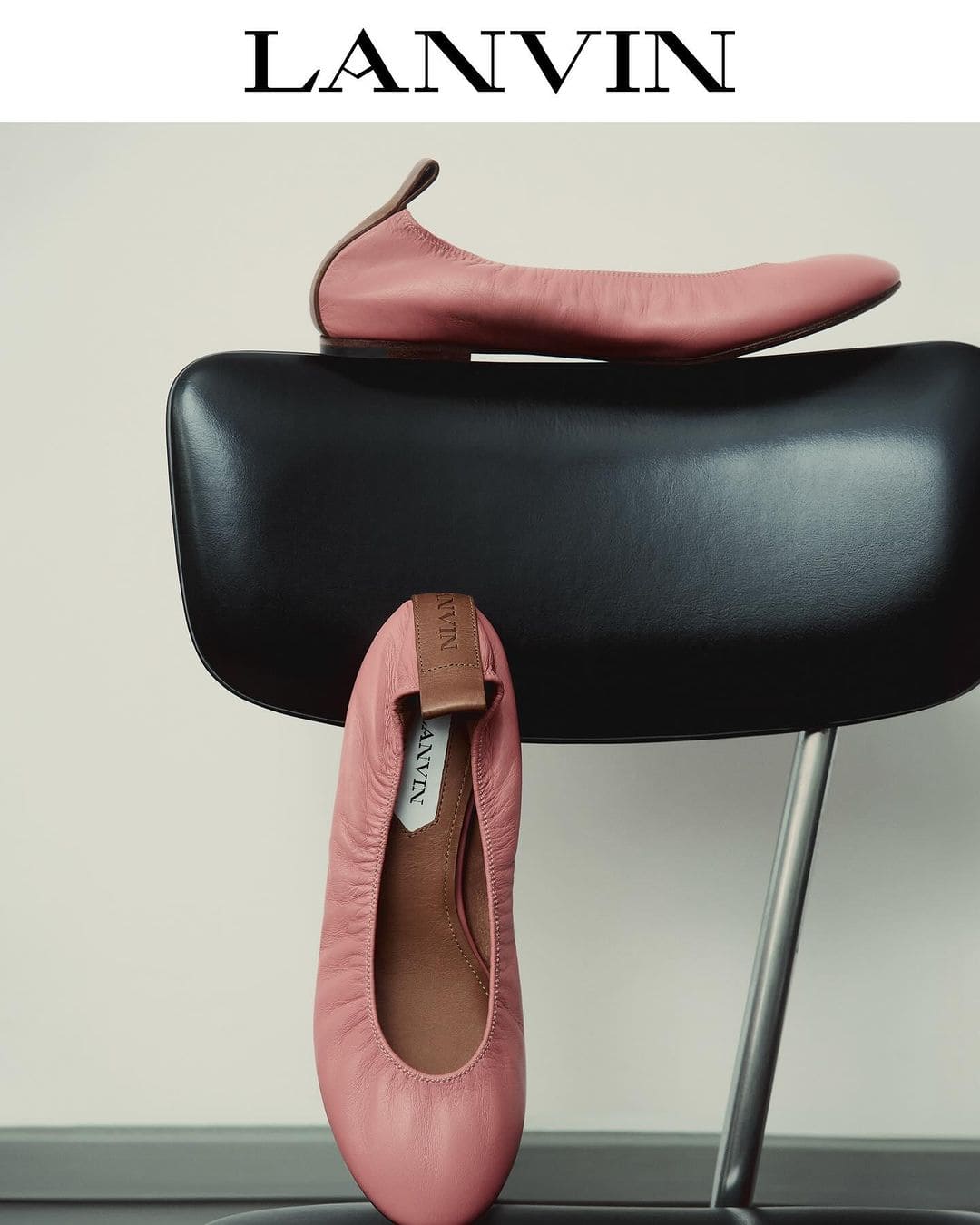 Elegant Lanvin ballet flats in pink leather, positioned on a modern black chair against a neutral backdrop. High-fashion footwear.