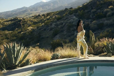Model standing by a swimming pool in desert landscape wearing yellow patterned loungewear