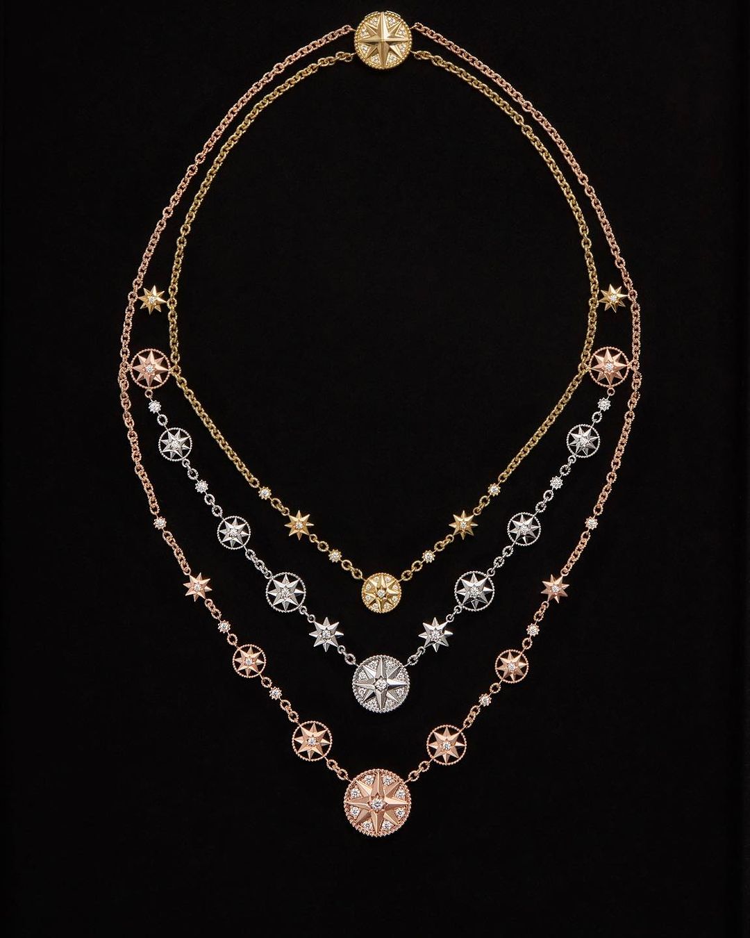 Three delicate gold necklaces with compass rose pendants and star accents, displayed against a dark background, showcase jewelry design.