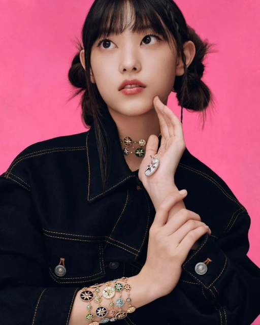 Portrait of a young Asian woman with pigtails wearing a black jacket, necklace, and bracelet against a pink background in a studio setting.