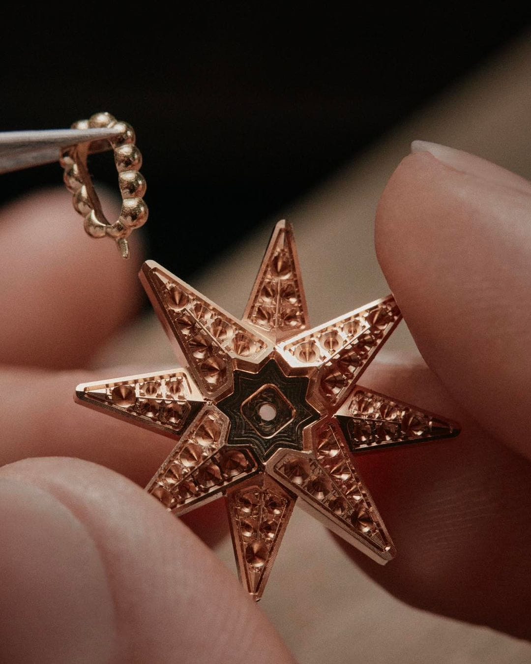 Close-up of a person holding a rose-gold star-shaped pendant with intricate geometric patterns and a small gold ring attachment.